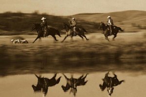 Konrad Wothe - Cowboys riding Horses with dogs running beside pond, Oregon - Sepia